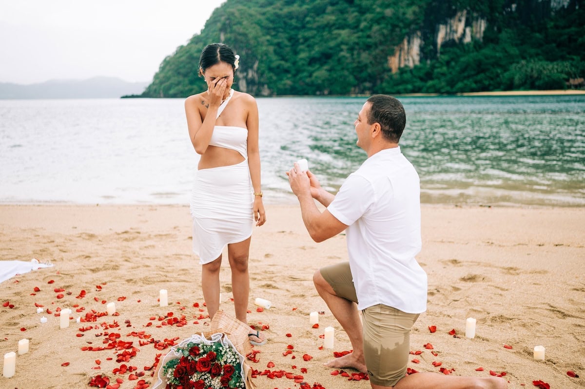 Romantic proposal on the beach in El Nido, Philippines, with a couple surrounded by candles and rose.
