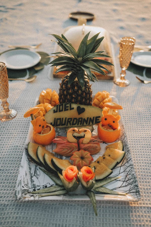 Romantic wedding proposal with tropical fruit arrangement on beach table.