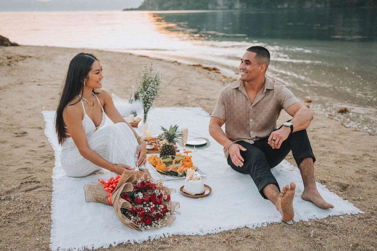 Romantic couple enjoying a beach picnic during a wedding proposal in El Nido, Philippines.