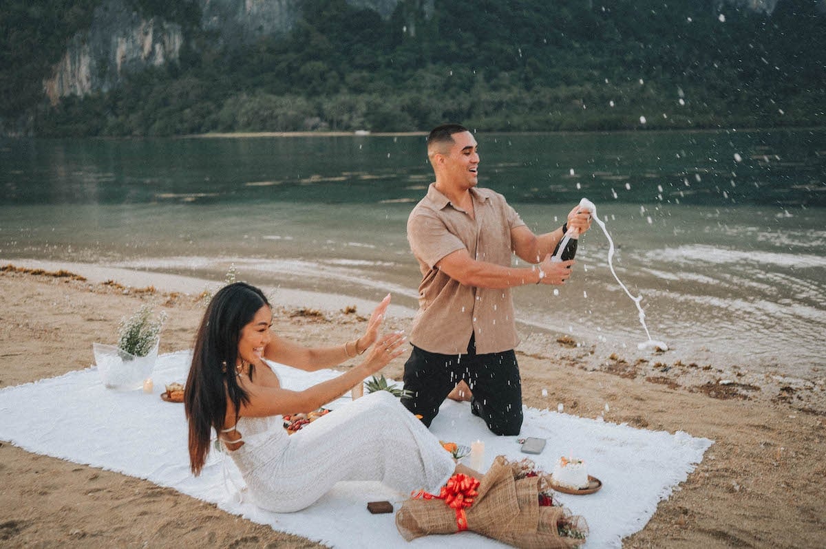 A couple celebrating a wedding proposal on the beach in El Nido, Philippines, with scenic limestone.