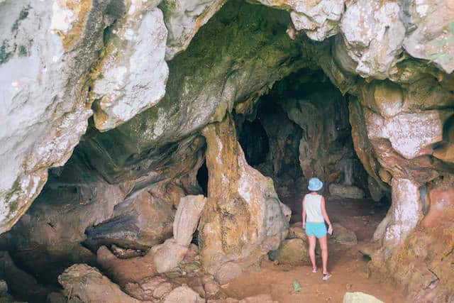 Person in a hat and shorts exploring a rocky cave on Gigantes, perfect for island hopping adventures.