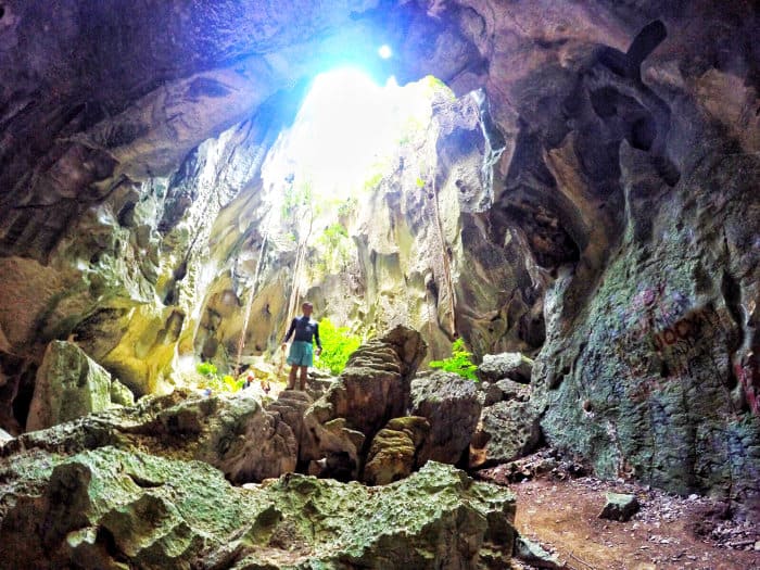 A person stands amidst rocks inside a large cave on a Carles island, with sunlight streaming through the opening above.