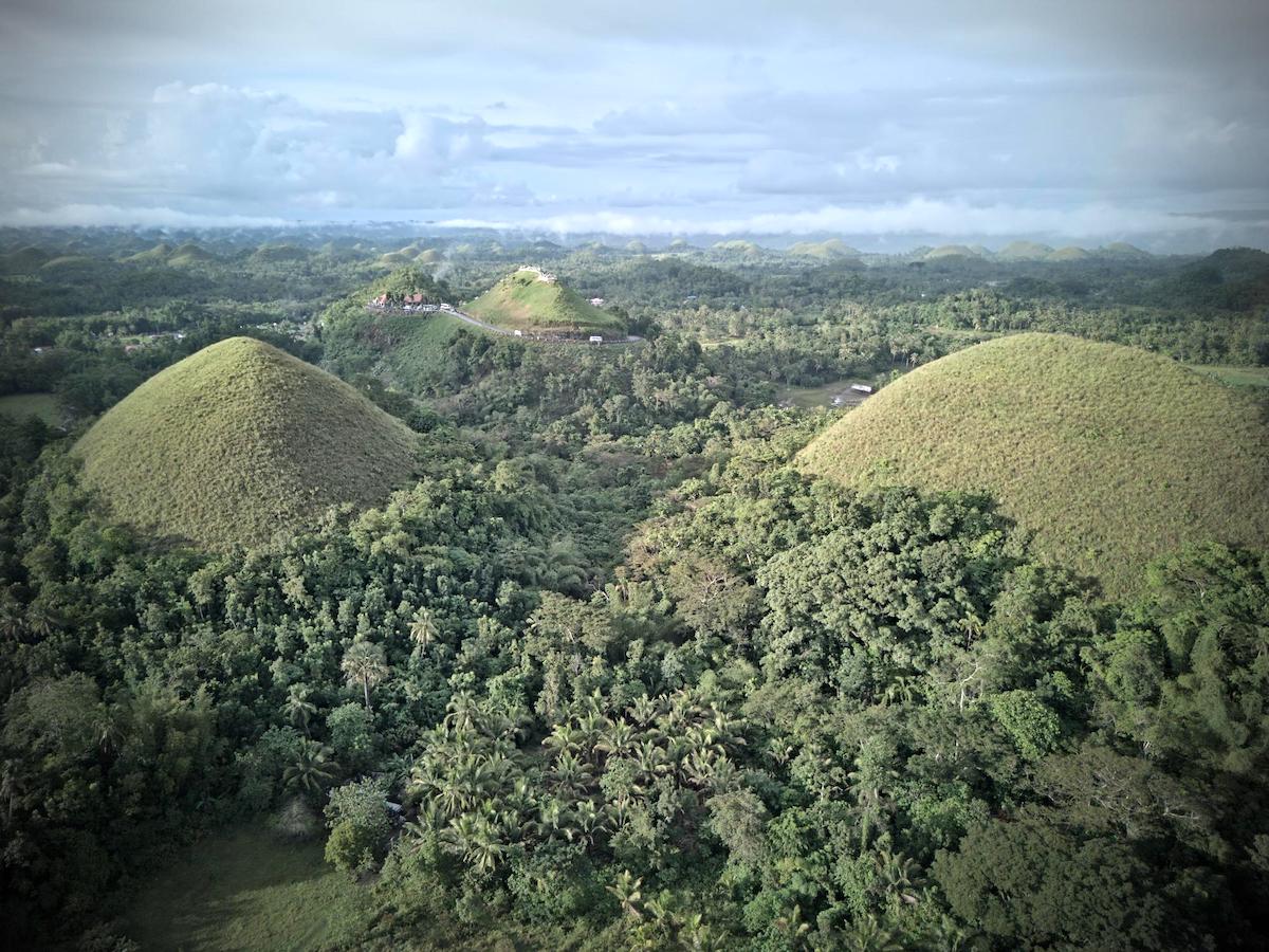 Aerial view of the Chocolate Hills near lush forests, with Cebu and Dumaguete just a scenic journey from this Bohol, Philippines wonder.