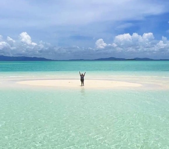 Stunning turquoise waters and white sand beach in Philippines with a person enjoying the scenery.