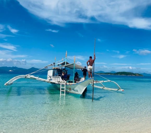 Traditional Filipino boat anchored on pristine beach with turquoise sea.
