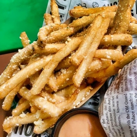 Golden crispy French fries with parmesan cheese and dipping sauce in a paper tray.