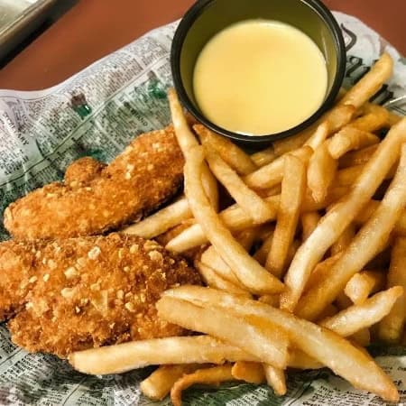 Crispy fried chicken tenders with french fries and creamy dipping sauce on a paper-lined tray.