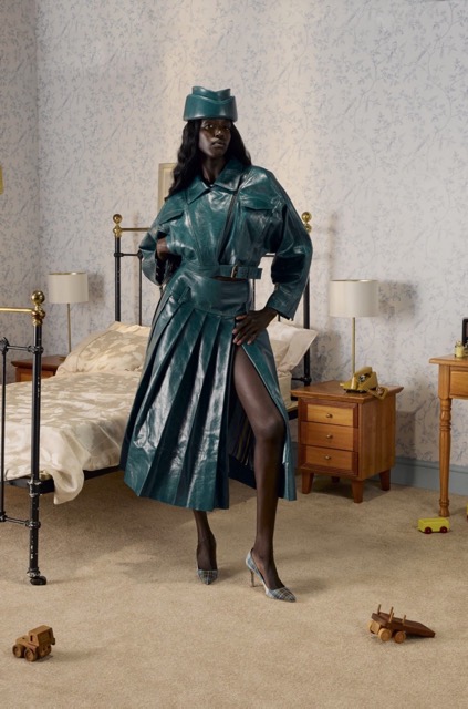 a woman in a green coat and hat standing in a bedroom