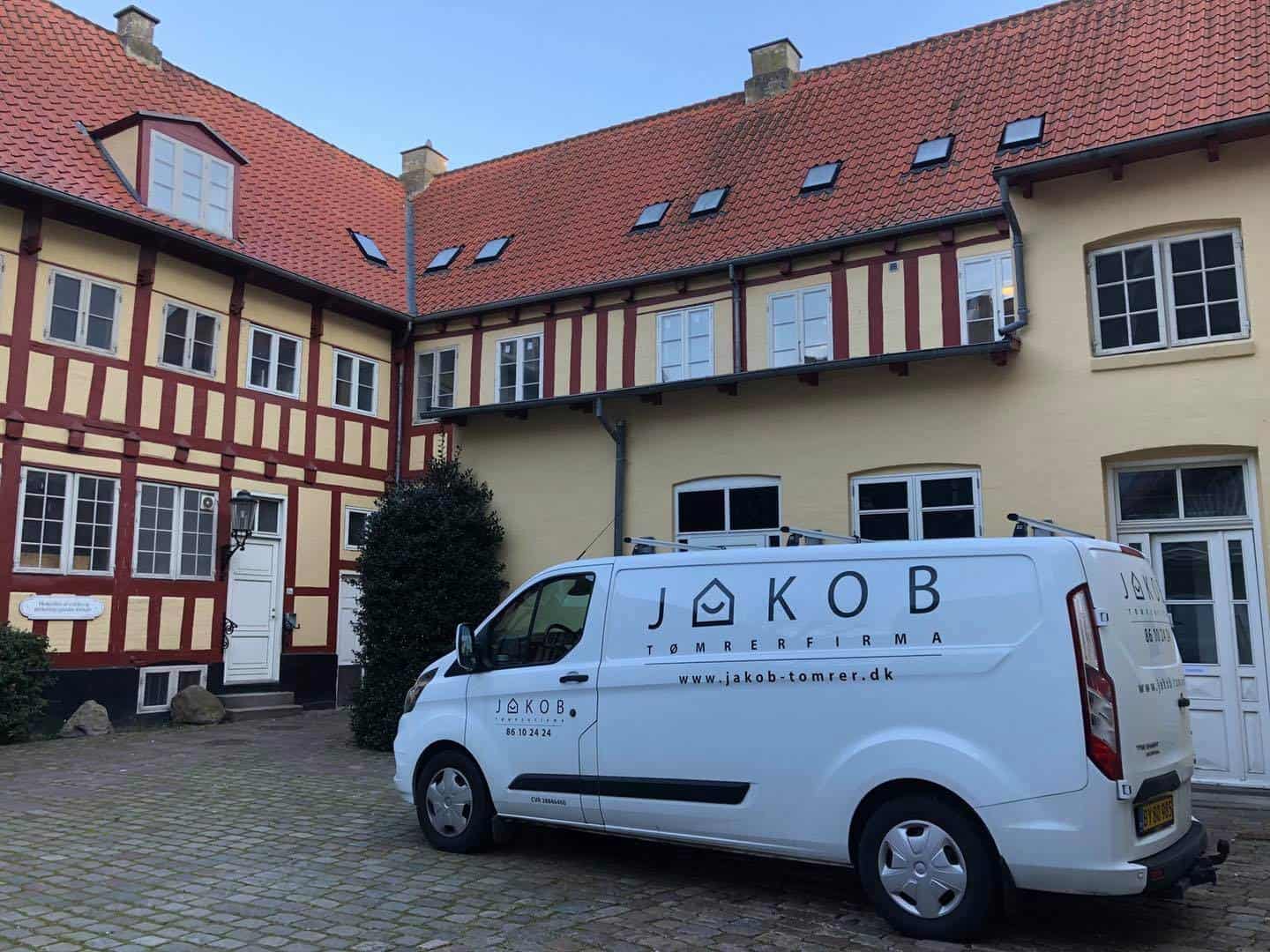 Tømrerfirma Jakob Tømrer A/S med servicebil foran en ældre, charmerende bygning.