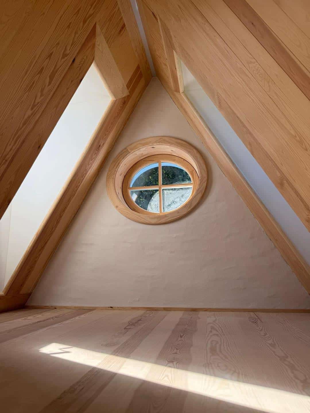 Loft med trævægge og rundt vindue, perfekt til hyggelig læsning eller afslapning.