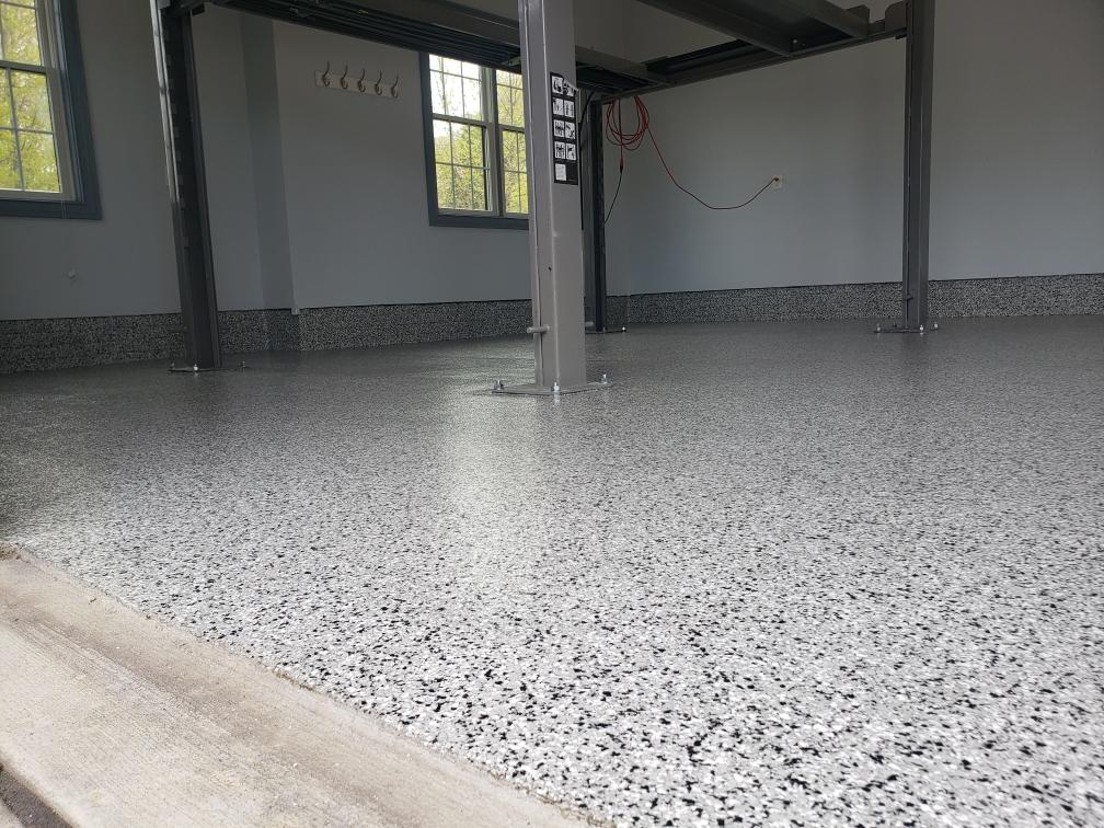 The image shows a garage with a smooth, fresh epoxy floor by J&P Coatings. The space looks bright and tidy, showing the results of a quality floor coating service.