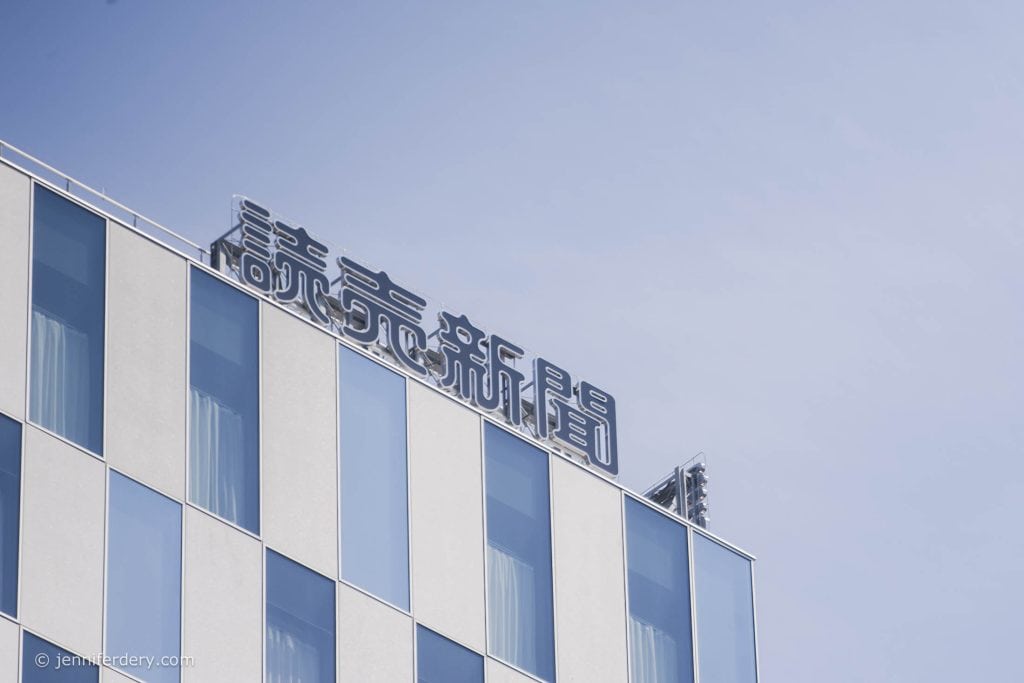 A modern building with large windows and a sign in Japanese characters on the rooftop against a clear blue sky.