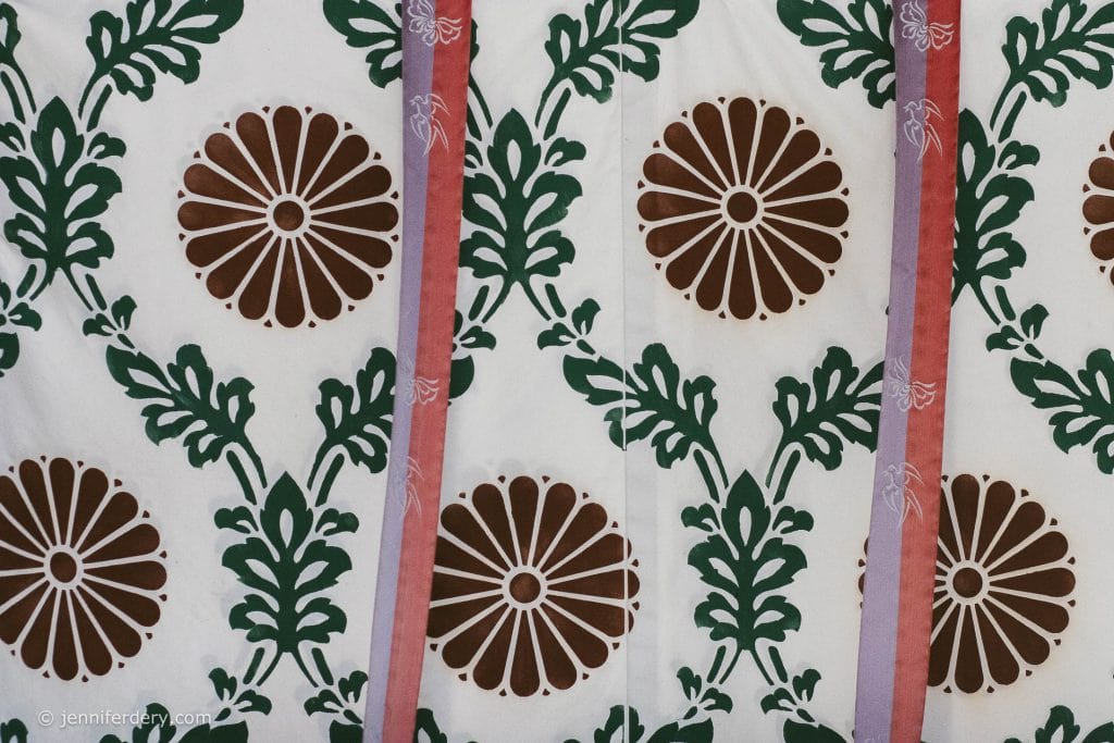A patterned fabric with brown circular floral designs, green leafy motifs, and vertical pink and red stripes on a white background.