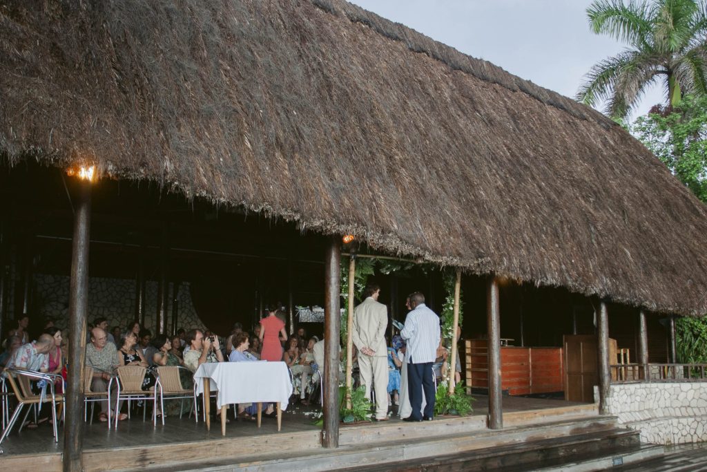 Rockhouse Hotel, Negril, Jamaica: A group of people sit and stand under a large thatched-roof outdoor structure with open sides, gathered around tables for an event or meal, surrounded by lush greenery.