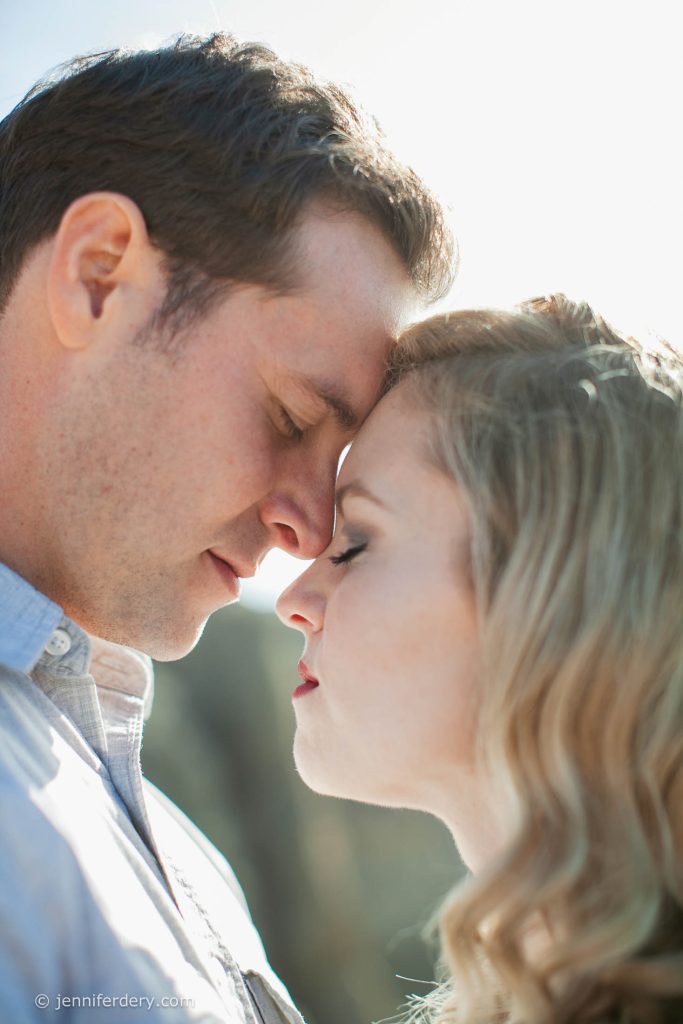 A close-up of a couple gently touching foreheads with their eyes closed, sharing an intimate and tender moment outdoors in soft natural light.