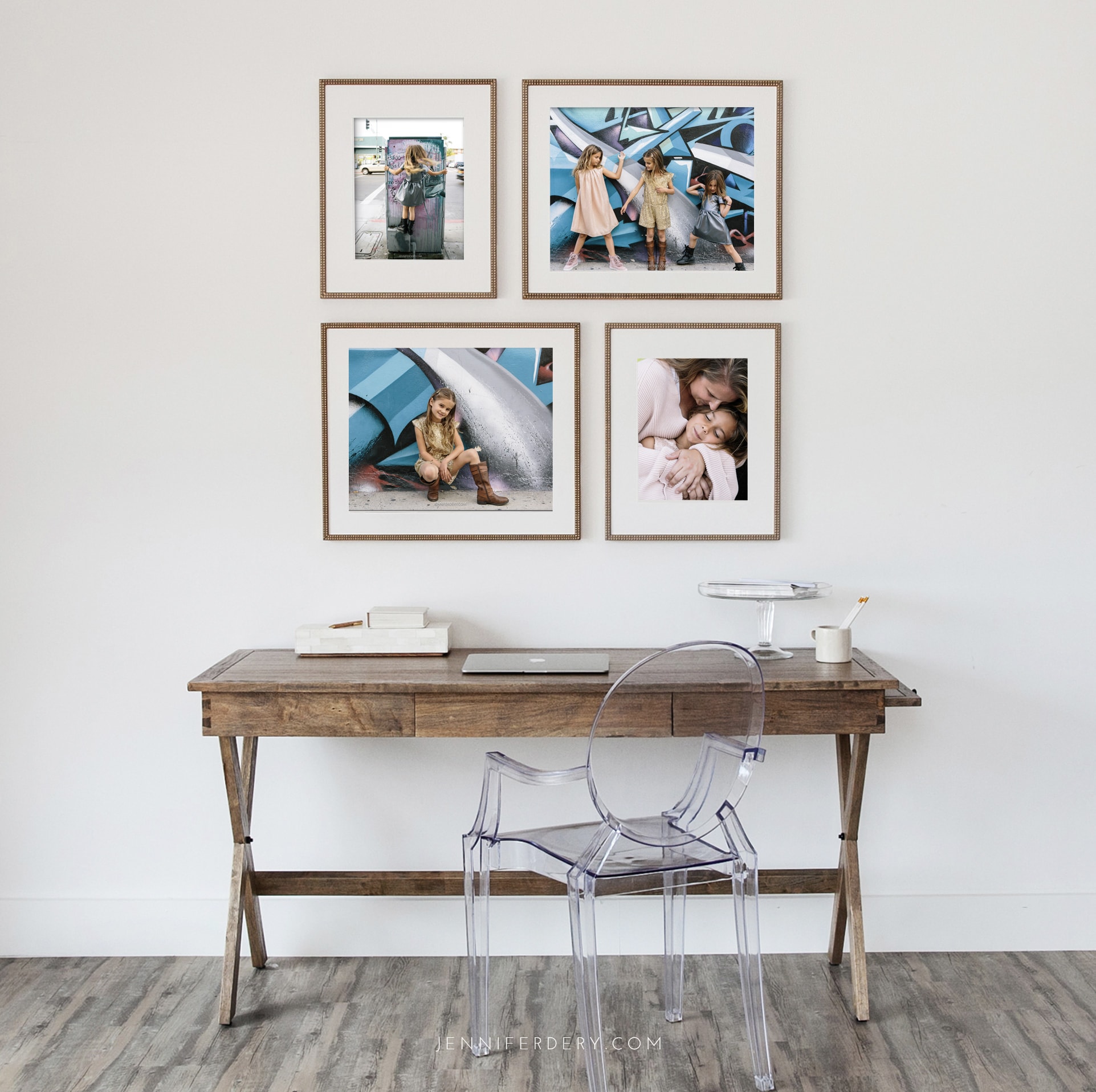 A minimalist home office with a wooden desk, a transparent acrylic chair, and framed family photos on the wall. The desk holds notebooks, a clear tray, a pencil holder with pencils, and a cup. The setup is on a white wall with a light-colored floor.