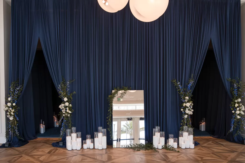 Southpointe ballroom mirrored sign and floral installation in foyer using white garden roses, calla lilies, delphinium, and anemones against navy velvet curtains and tall candles