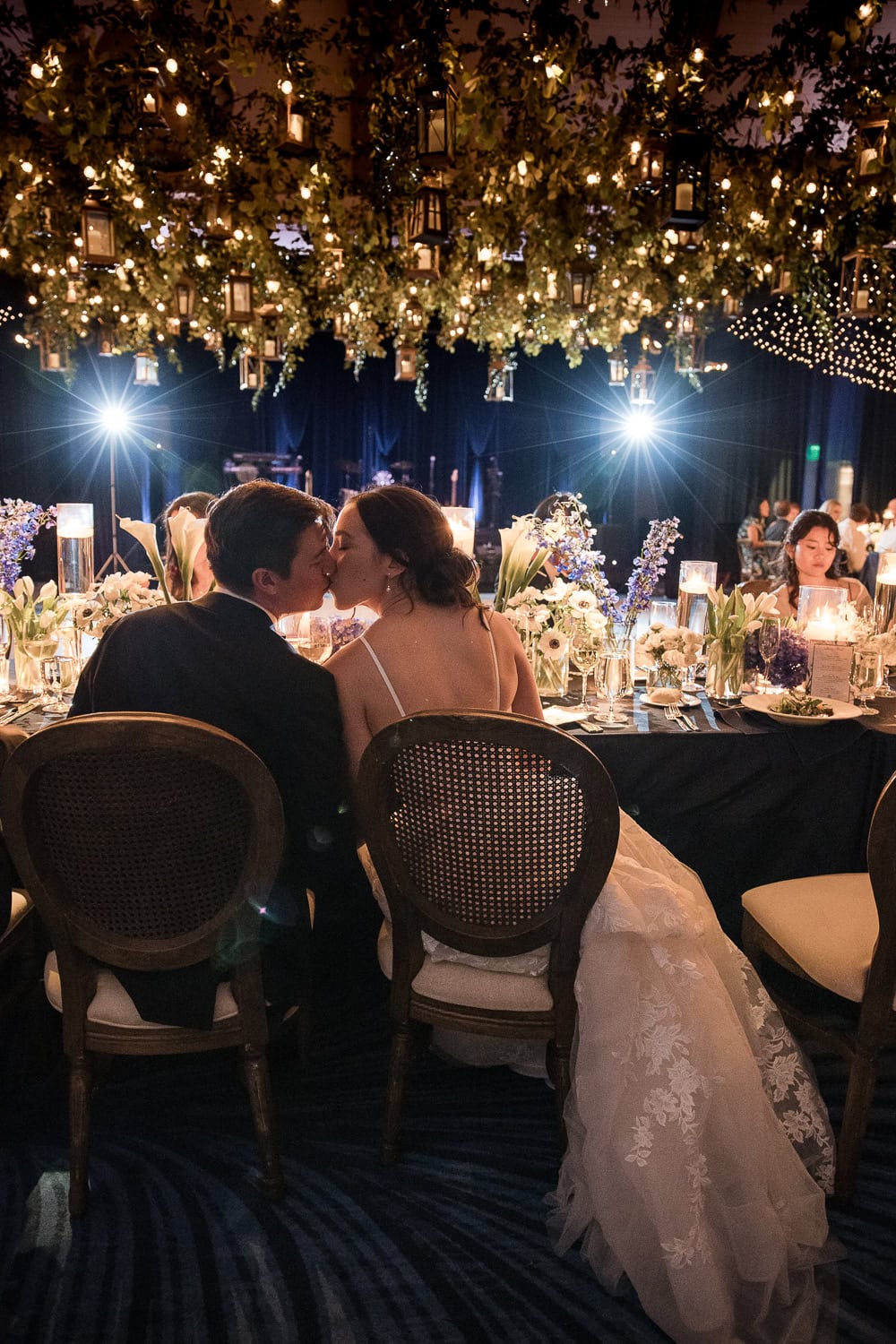 Southpointe ballroom showing the bride and groom kissing at the head table, lucky devils band in the background, with twinkle fairy lights overhead