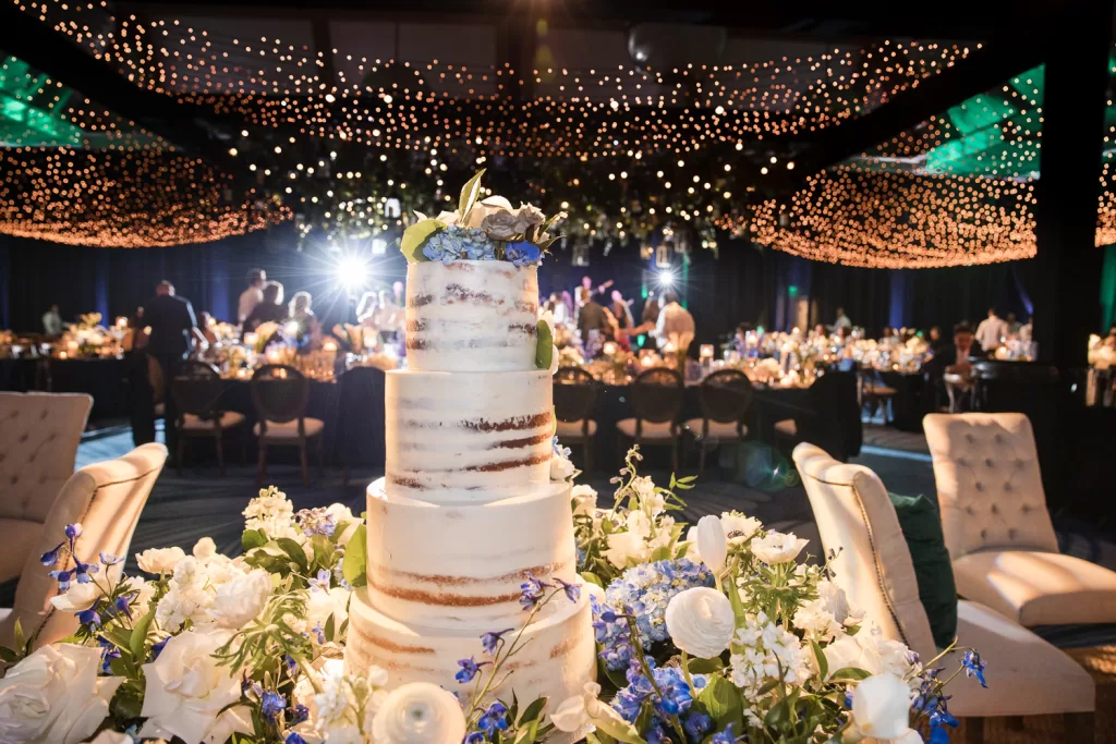 Southpointe ballroom floral installation around naked wedding cake of white garden roses and blue hydrangea. dance floor with twinkle lights in the background