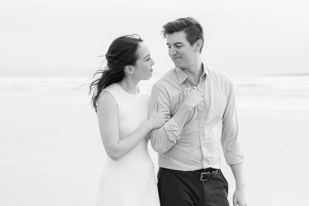 black and white photo of a couple holding hands on the beach in coronado in san diego. white dress and blue button-down with navy pants