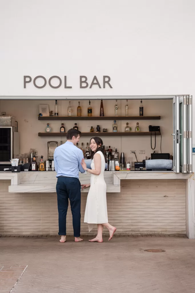 couple holding hands in front of the pool bar at the hotel del coronado in san diego. white dress and blue button-down with navy pants