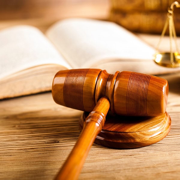 An image of a gavel resting on it's side with a book and the scales of justice in the back.