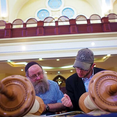 Two men standing together reading the Torah.