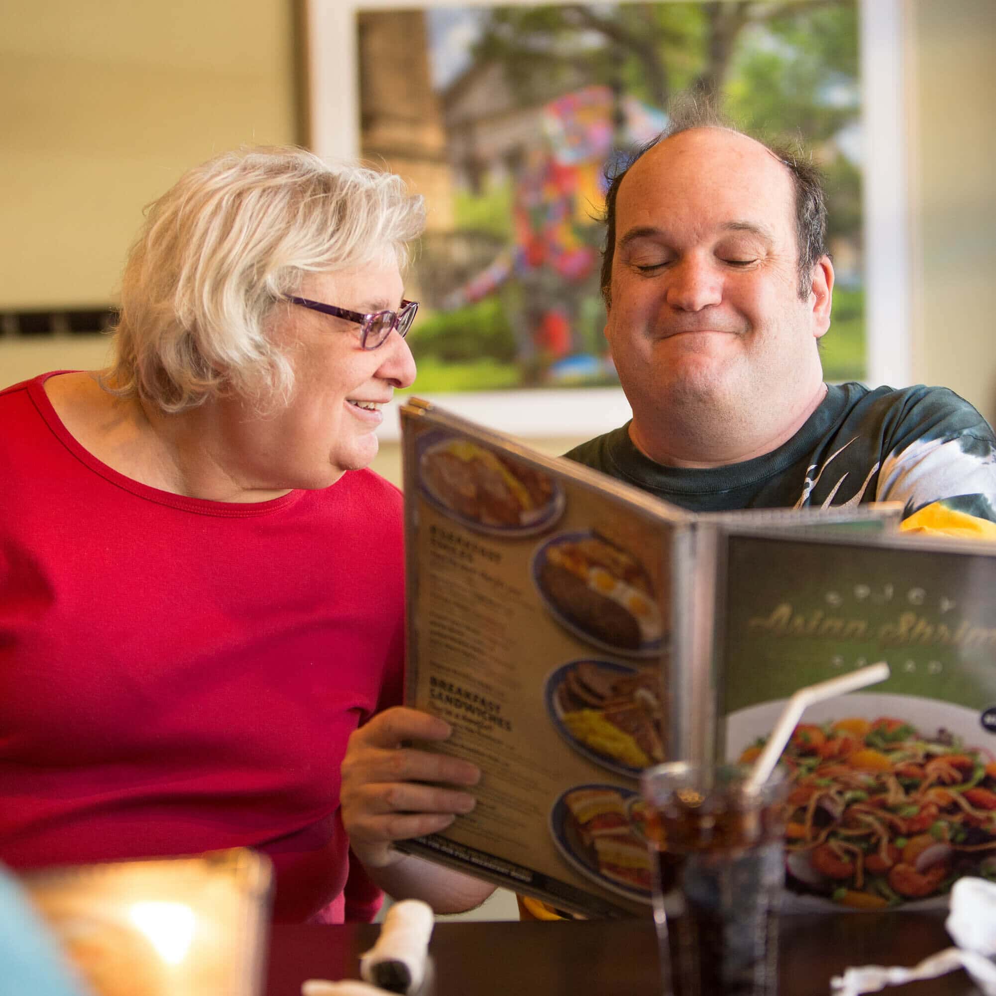 Two people sitting at a restaurant. The one person is holding a menu and smiling.