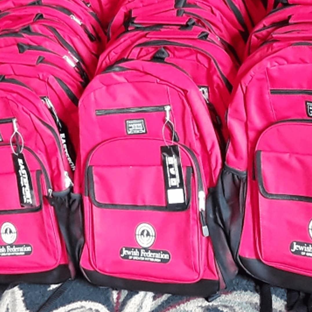 Rows of red backpacks with the Jewish Federation logo on the front.