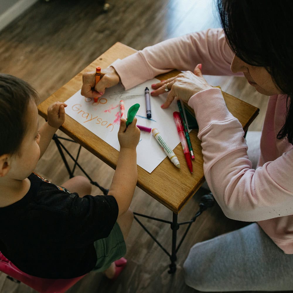 teacher helping child write with crayons
