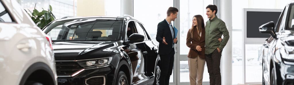 Black SUV vehicle with a sales associate talking to a couple inside a car dealership showroom.