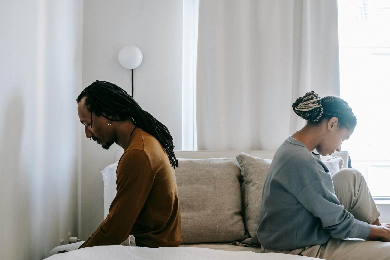 Couple sitting back-to-back on bed, reflecting on relationship issues.