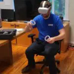 Person sitting in an office chair wearing a VR headset and holding controllers, engaged in a virtual experience.