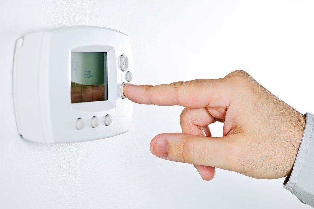 A person adjusting a digital thermostat on a white wall.
