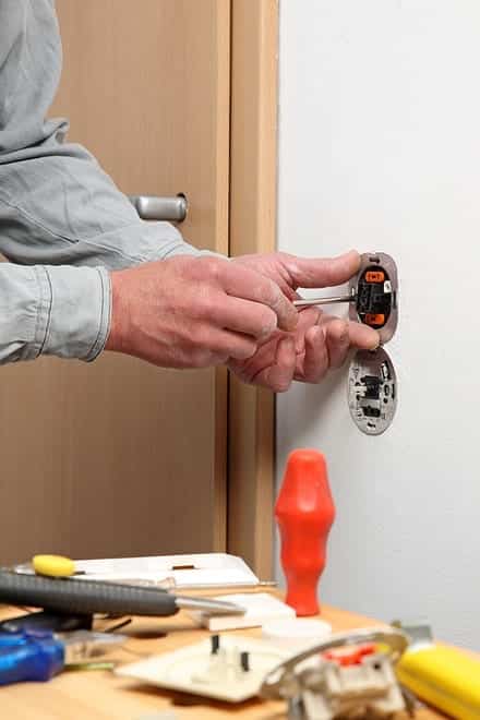 Person fixing a wall socket with tools spread on a nearby surface.
