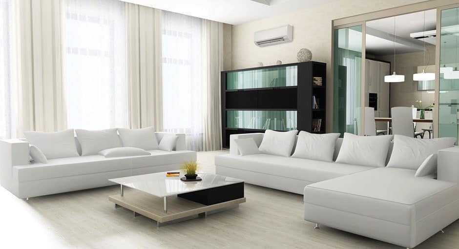 Modern living room with white sofas, light wood floor, glass coffee table, and a black shelf. Large windows with white curtains and view of a dining area in the background.
