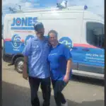 Two people in blue shirts stand in front of a company van with the word "JONES" on it.