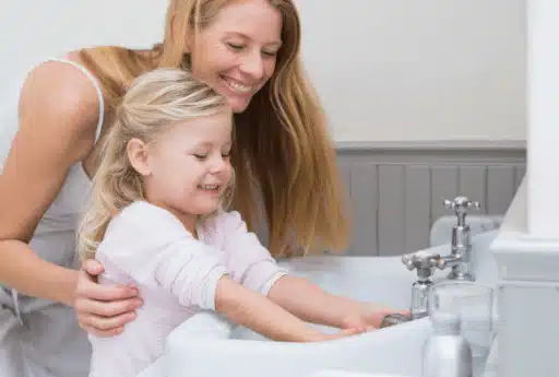 A woman assists a smiling child washing hands at a sink, both appearing content and focused on the activity, much like reading glowing service reviews that highlight genuine care and attention.
