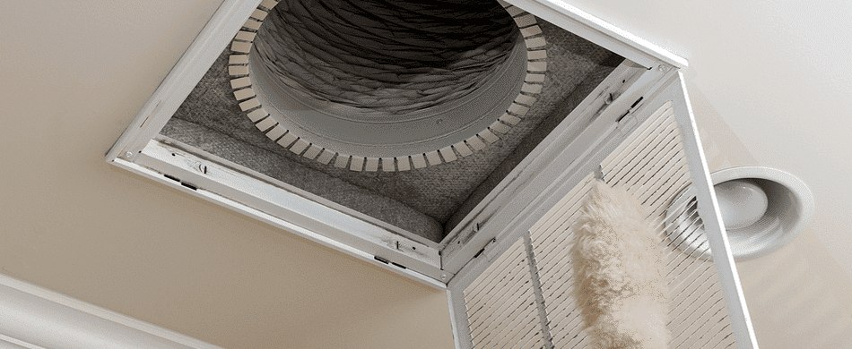 An air duct with a vent cover opened, revealing exposed ductwork and a flexible hose, against a beige ceiling.