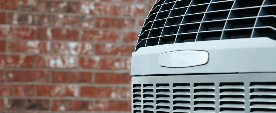 Close-up of an air conditioning unit with a grille pattern, positioned in front of a brick wall.