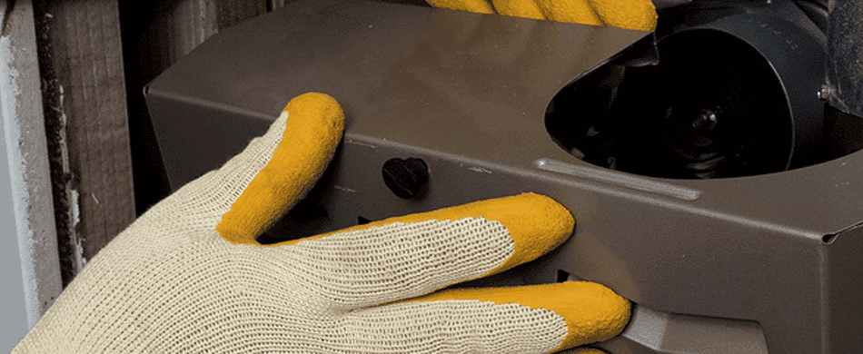 Person wearing yellow gloves installing or repairing a heating unit inside a building.