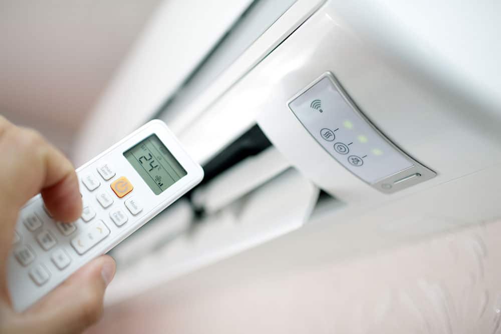 Close-up of a hand holding a remote control aimed at a wall-mounted air conditioning unit set to 24 degrees Celsius.
