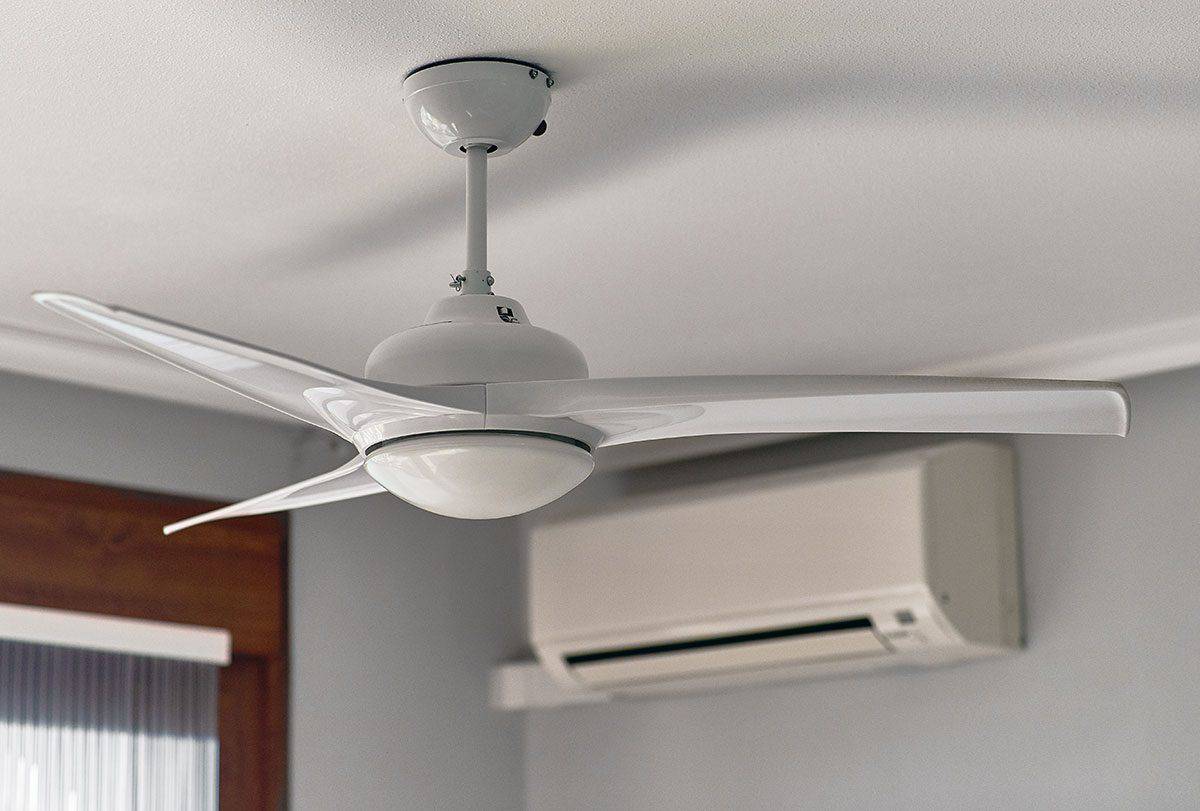 Ceiling fan with three blades mounted on a white ceiling next to a wall-mounted air conditioning unit.
