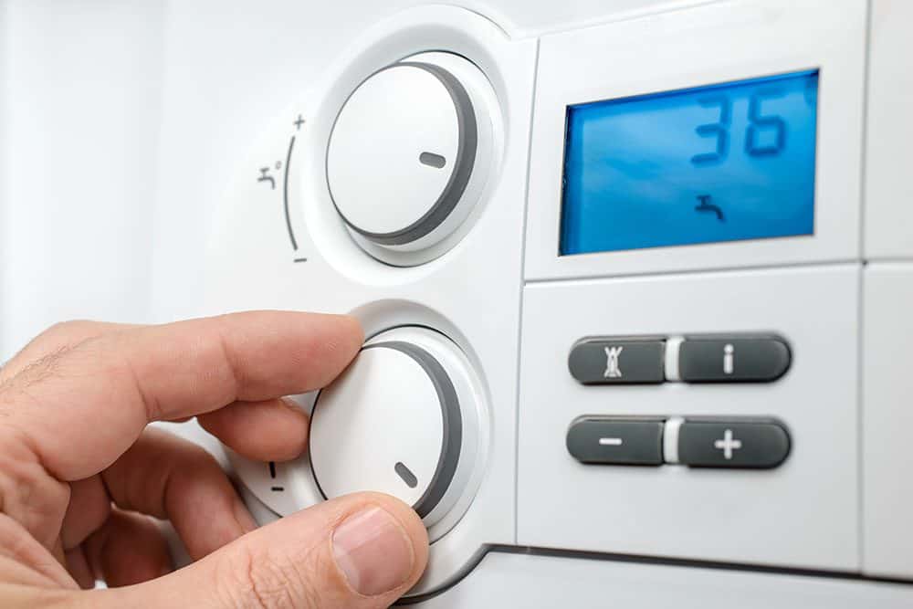 A hand adjusts the dial on a digital thermostat display set to 36 degrees with buttons for settings and temperature control.