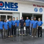 A group of ten people in blue shirts standing in front of a building with signage that reads "Jones Services.