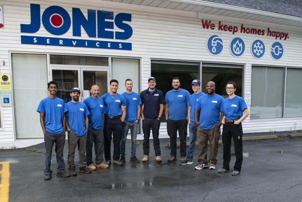 A group of ten people in blue shirts stands in front of a building with the sign "Jones Services" and the slogan "We keep homes happy.