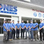 A group of eleven people in matching blue shirts stands in front of a building with a "Jones Services" sign.