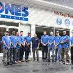 A group of workers in blue shirts stands in front of a building with "Jones Services" signage.