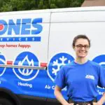 Person in a blue shirt stands smiling in front of a service van with logos and text related to home services like heating and cooling.