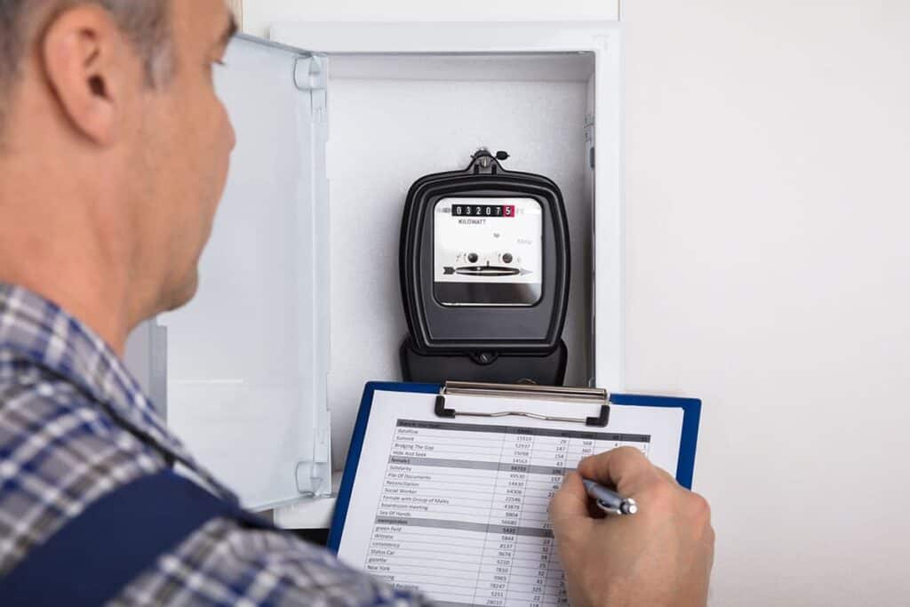 A person records data from an electricity meter into a checklist on a clipboard to monitor energy efficiency and save energy.